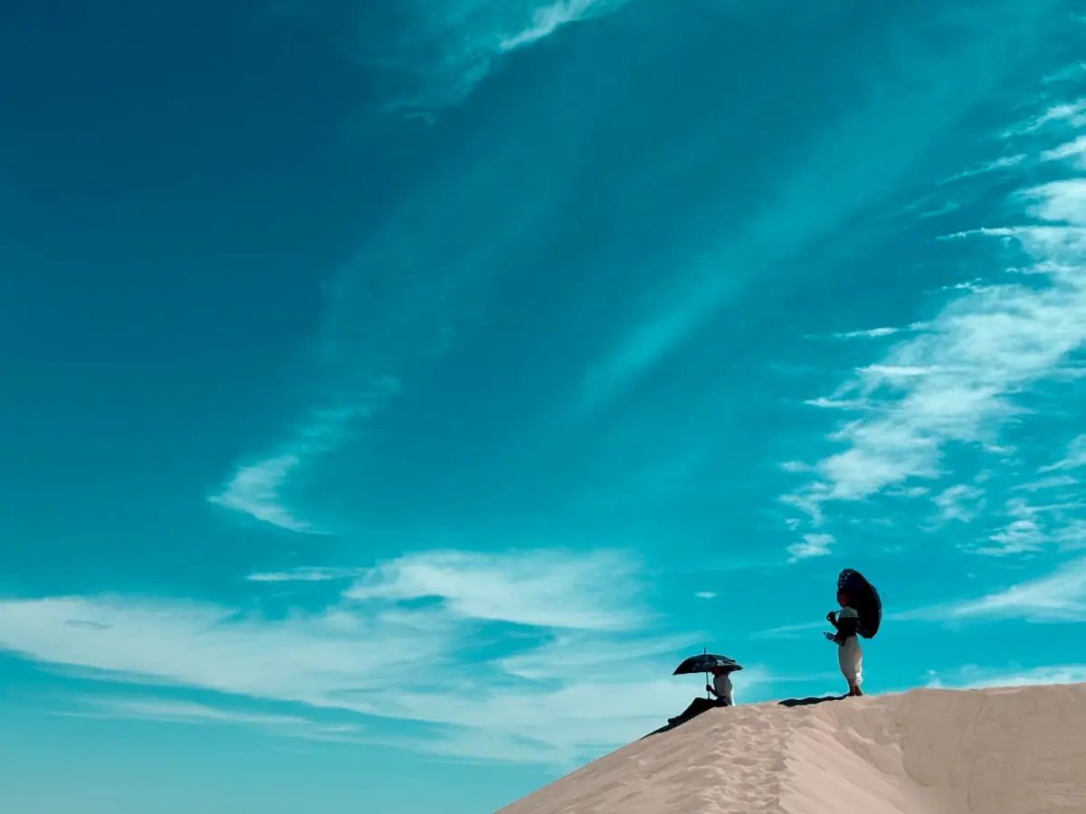 Two travellers with umbrellas on the crest of the Khongor dunes