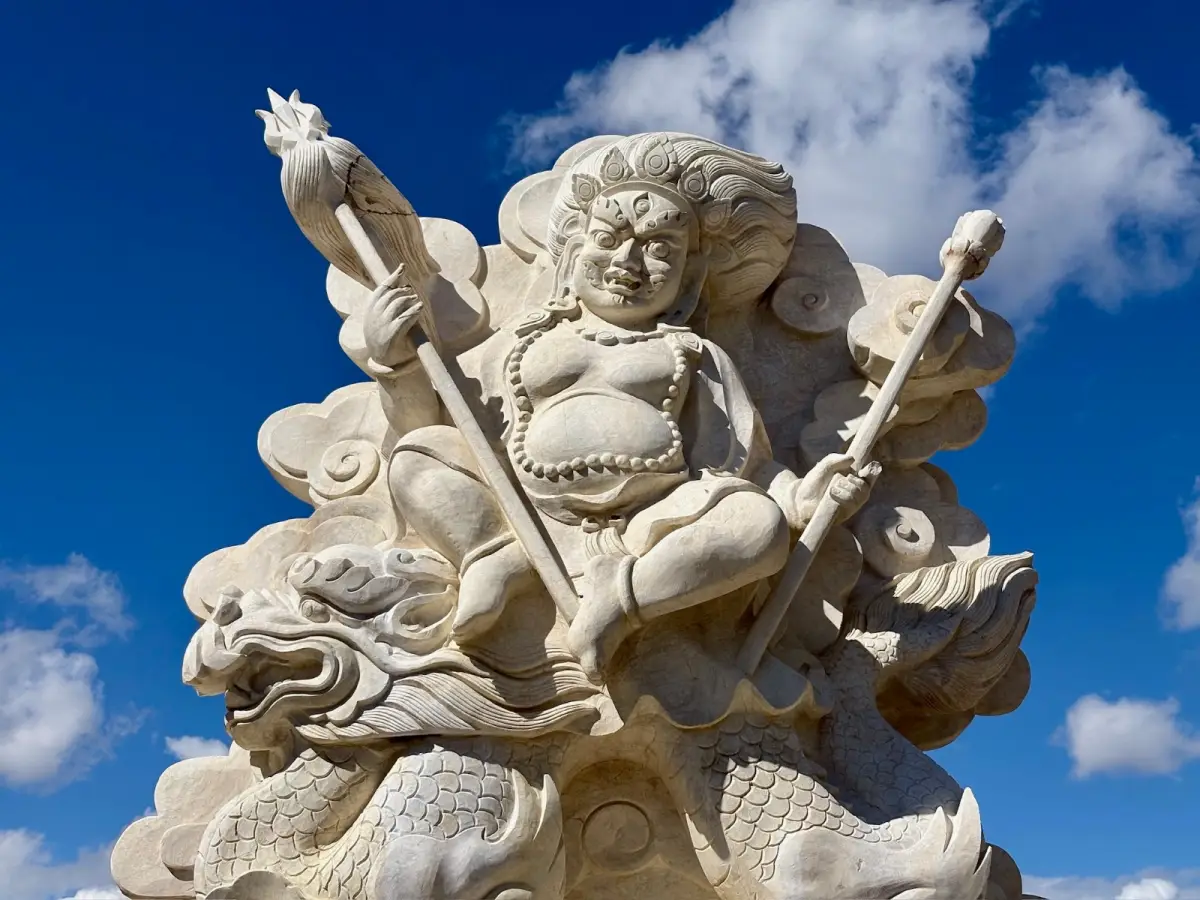 A carved white stone deity riding a dragon against a deep blue sky